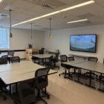 Image of the classroom taken from the back of the room showing clusters of tables and chairs.