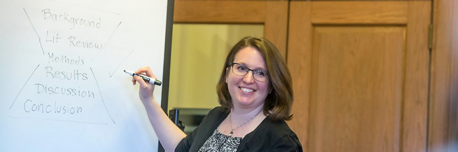 Smiling instructor looks out while writing on a whiteboard
