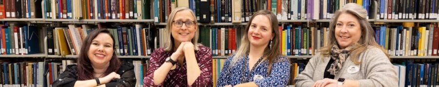 library employees smiling in front of shelves of books