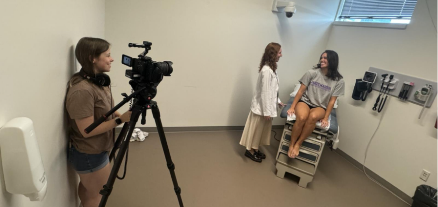 young woman behind camera filming two students in a medical exam room
