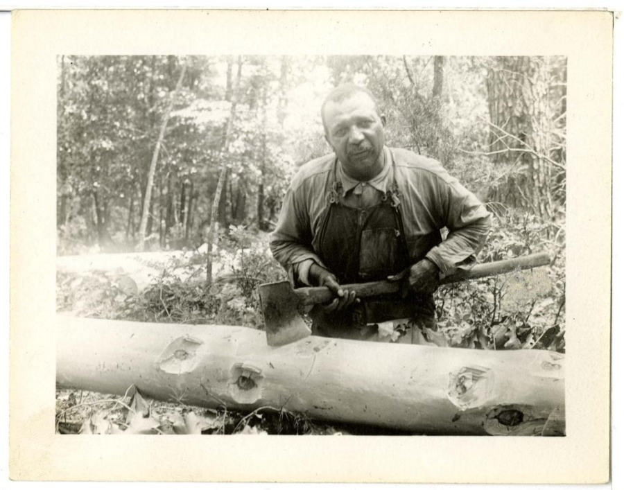 a black and white photograph of a man standing over a log holding an ax