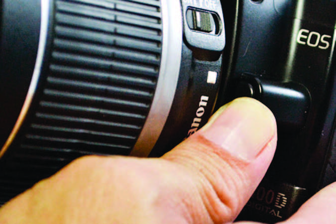 A thumb pushes the lens release button on a DSLR camera.