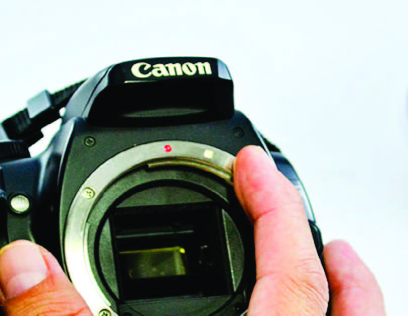 Fingers indicate the white/red lens alignment dots on a DSLR camera with no lens.