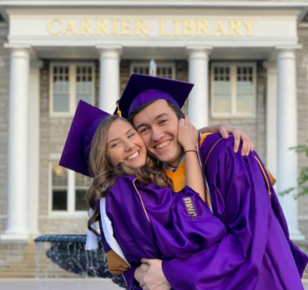 Jess and Cameron in graduation gowns hugging in front of Carrier Library
