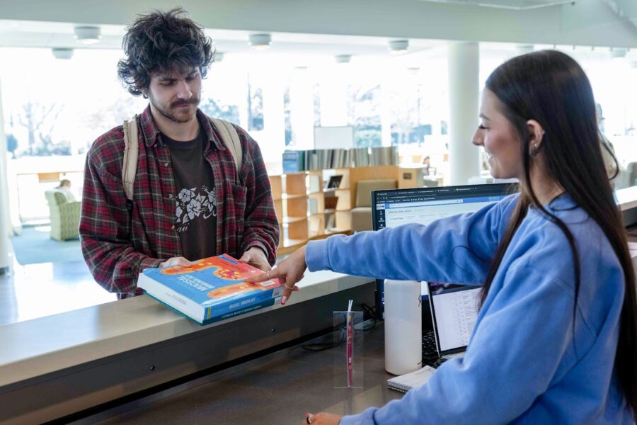 student picking up textbooks from a library desk