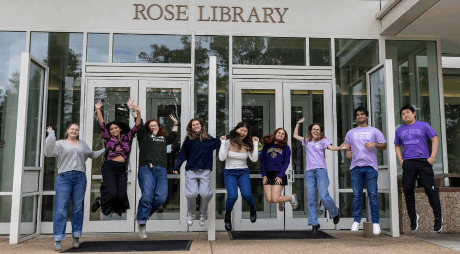 students jumping and smiling in front of rose library at JMU