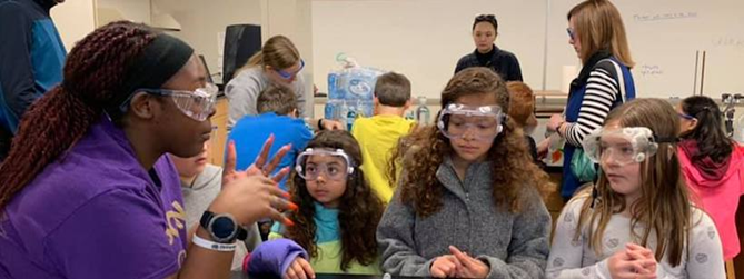 photo of JMU student and elementary students wearing safety goggles