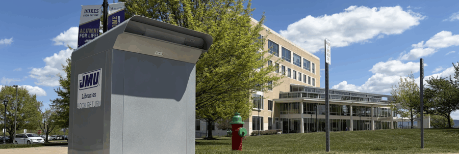 JMU's rose library in the background and the book drop near rose library int the foreground, the sky is blue with a few white cloud.