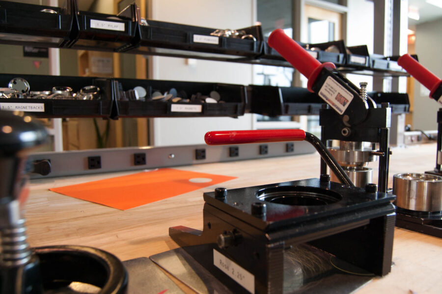 Red-handled button maker press on a workbench.