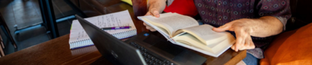 hands holding a book in front of a computer