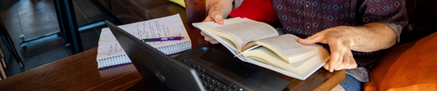 hands holding a book by a laptop