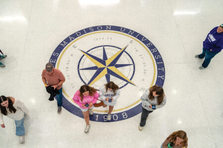 Overhead view of people walking across purple and gold compass rose floor artwork.
