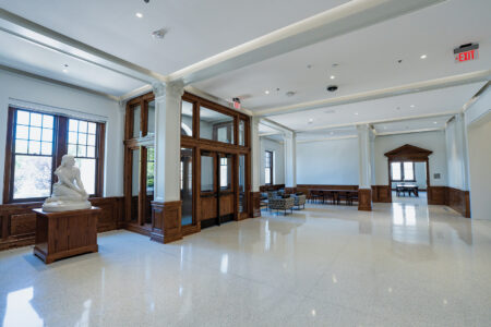 Well-lit entrance lobby with high ceilings, polished white floors, varnished wood trim, and Joan of Arc statue.