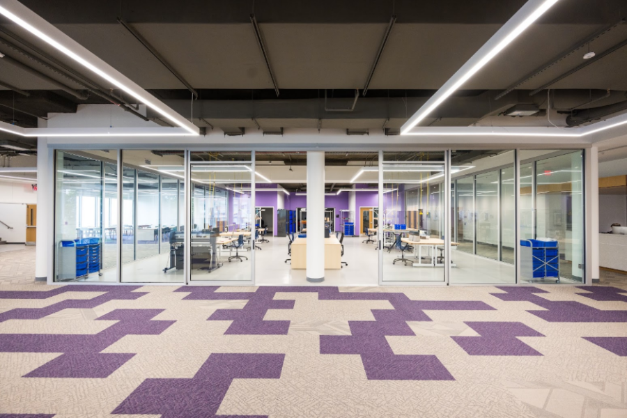 glass-walled room filled with tables, chairs, and makerspace equipment