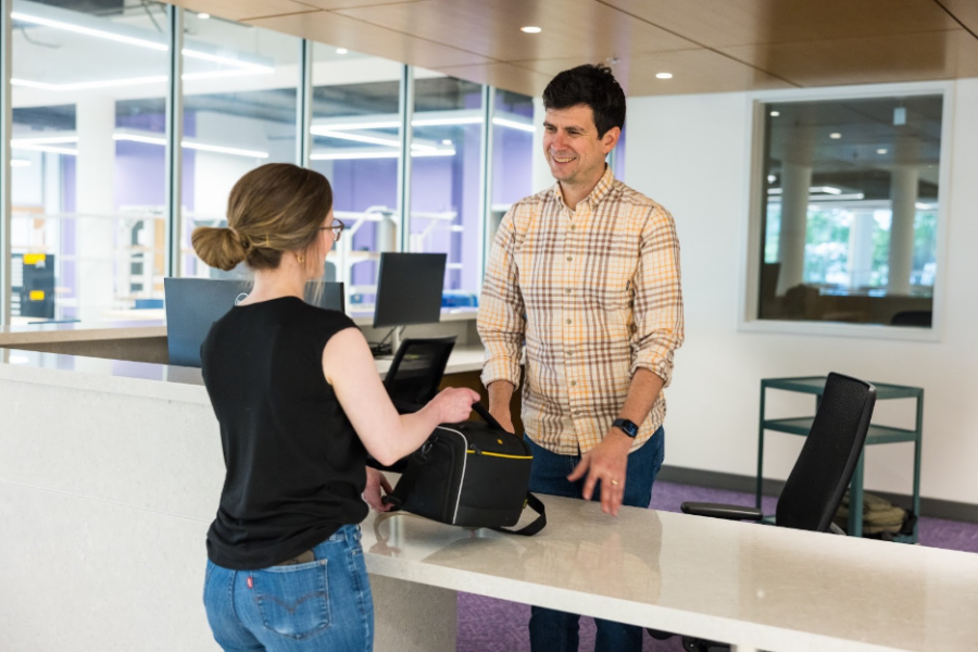 Libraries employee behind a desk smiling as a woman picks up a camera bag
